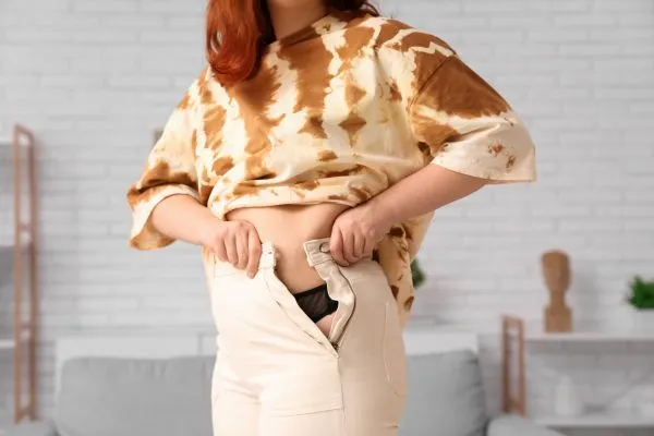 Image of woman trying to do her trousers up after pregnancy weight gain Corby