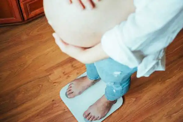 Image of woman weighing herself and experiencing weight gain through pregnancy Corby